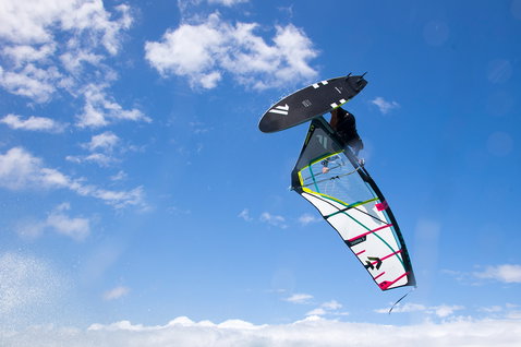 Fanatic FreeWave TeXtreme wave windsurf board during wave riding – rider airborne against blue sky
