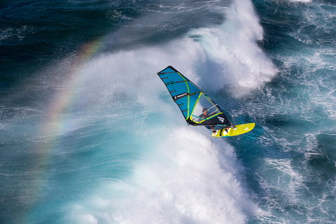 Fanatic Stubby TE Windsurf Waveboard beim Wellenreiten auf dem Ozean mit Regenbogen im Hintergrund