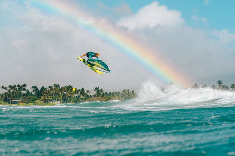 Fanatic Stubby TE Wave Windsurf-Board beim Wellenreiten mit Sprung über tropischem Ozean mit Regenbogen
