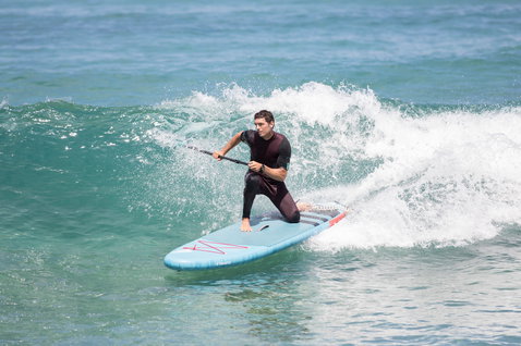 Duotone Fly Air inflatable SUP board during wave riding on the ocean in light blue and red
