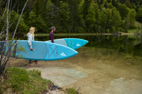 Fanatic Ray Air inflatable touring SUP board in teal carried by two people at a mountain lake