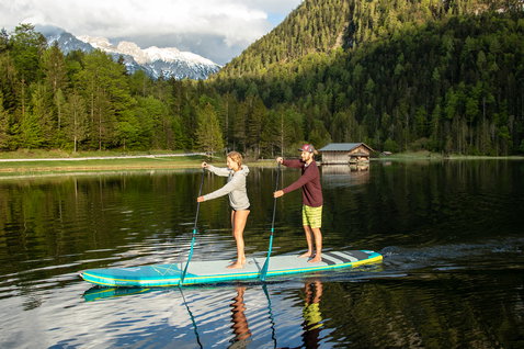 Duotone Tandem Air Premium inflatable SUP board with two riders paddling on a calm alpine lake
