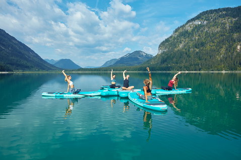 Duotone Fly Air Fit inflatable SUP board during SUP yoga on an alpine lake with five people