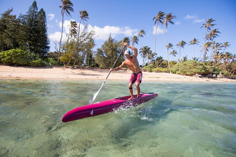 Planche de SUP de course Fanatic Strike Carbon lors d'une session de pagaie en lagune tropicale, magenta