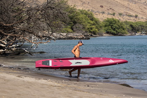Planche de SUP race Duotone Strike Carbon portée par un athlète sur une plage tropicale