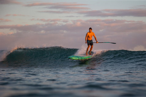 Duotone Fly Air Premium aufblasbares SUP Board beim Wellenreiten im Meer bei goldener Stunde