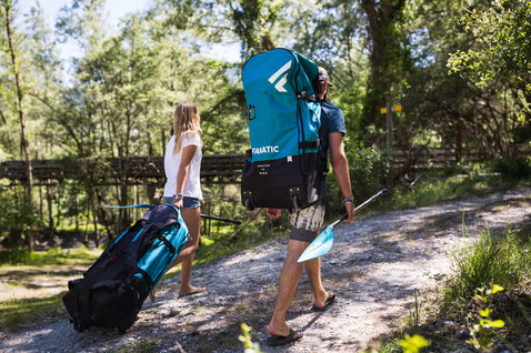 Fanatic Rapid Air Touring inflatable SUP bag in teal and black carried on trail through forest