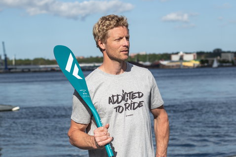 Fanatic Addicted To Ride men's short sleeve tee in heather grey during SUP at the waterfront