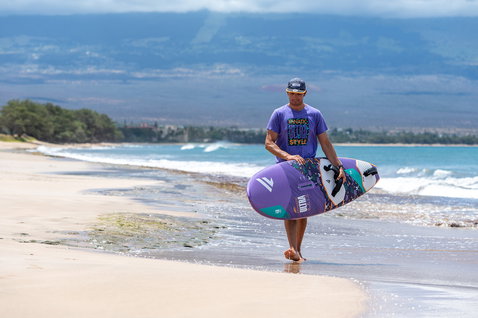 T-shirt unisexe Fanatic Ultra Style 40yrs en violet lors d'une promenade sur la plage avec planche de windsurf Fanatic