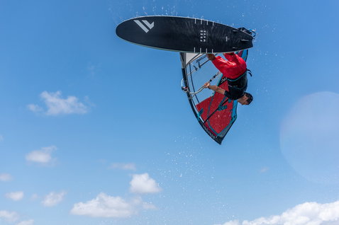 Fanatic FreeWave TeXtreme windsurf board during wave windsurfing with inverted aerial maneuver against blue sky