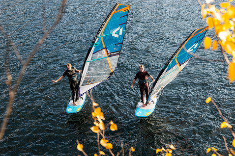 Fanatic Stingray LTD foil windsurf board during windsurfing on an autumn lake, aerial shot with two riders
