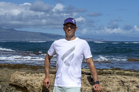 Fanatic Cap F cap in navy purple worn by athlete on rocky coastal shoreline