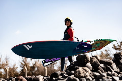 Fanatic Grip XS wave windsurf board in dark teal during wave riding at a rocky coastal location