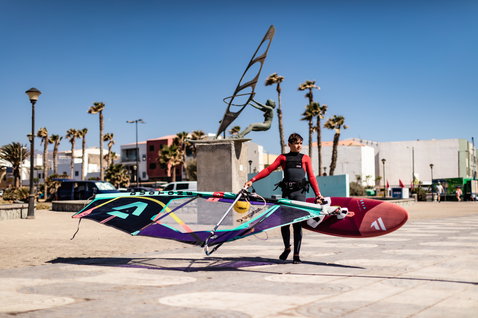 Fanatic Grip XS wave windsurf board carried by young rider on a sunny coastal promenade