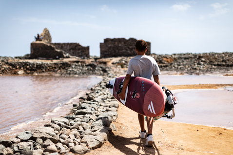Fanatic Grip XS wave windsurf board carried along a rocky coastal path in dusty rose
