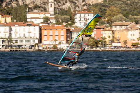 Fanatic Gecko Eco freeride windsurf board during windsurfing on a lake with alpine village backdrop