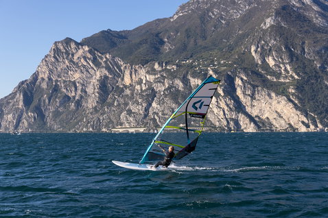 Fanatic Gecko HRS freeride windsurf board during windsurfing on Lake Garda with alpine mountain backdrop