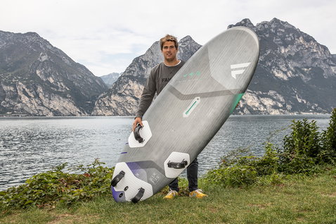 Fanatic Jag LTD windsurf board held by athlete at alpine lake with mountain backdrop