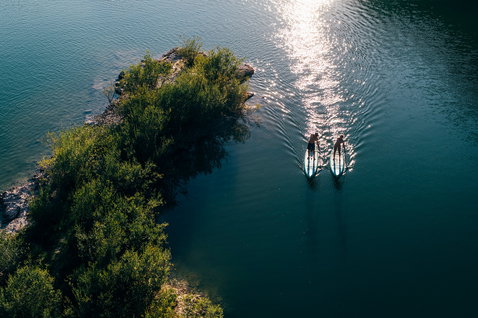 Duotone Ray Air Premium aufblasbares Touring SUP Board beim Paddeln auf einem ruhigen See, Luftaufnahme