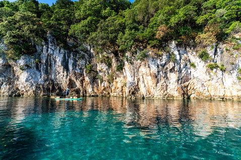 Duotone Ray Air Premium aufblasbares Touring-SUP beim Paddeln an felsiger Küste mit türkisem Wasser