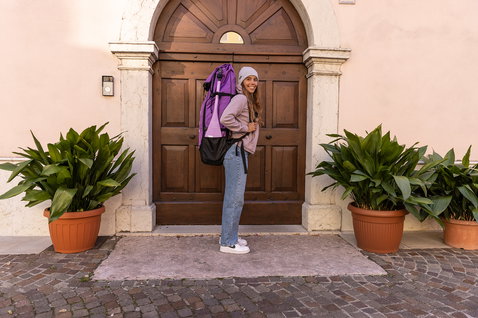 Duotone Diamond Air Touring Pocket inflatable SUP bag in purple worn as a backpack on a cobblestone street