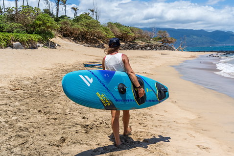 Fanatic FreeWave TE windsurf board in ocean blue carried on a tropical beach in Maui
