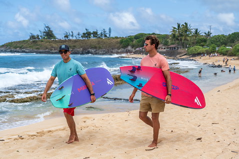 Fanatic Mamba TE Windsurf-Waveboard in lila-türkis mit zwei Athleten am Strand