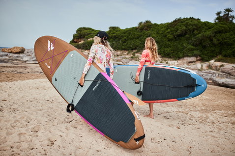 Planche SUP Duotone Fly Eco en placage bois avec lin et liège portée sur une plage de sable