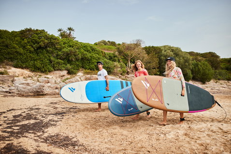 Planche SUP Duotone Fly Eco avec pont en placage bois portée sur une plage ensoleillée