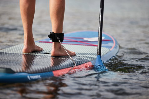 Détail du pont du SUP Fanatic Fly avec leash de cheville et pagaie carbone sur l'eau