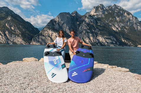Fanatic Blast LTD freeride windsurf board in white-blue and dark navy at alpine lake with two athletes