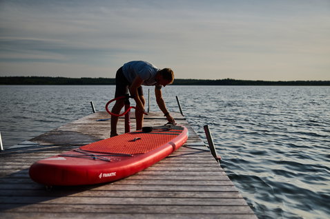 Duotone SUP Fly Air inflatable SUP board in red being prepared on a lake dock at golden hour