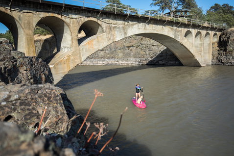 Duotone SUP Diamond Air inflatable SUP board during stand up paddling on a river beneath a stone arch bridge