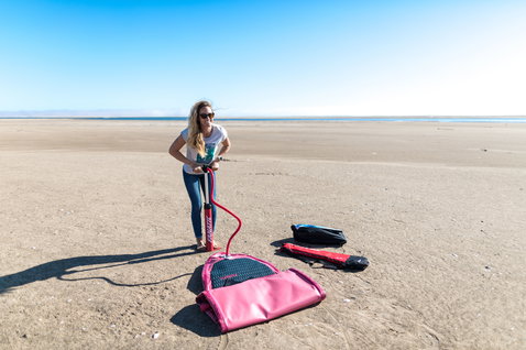 Fanatic Diamond Air inflatable SUP board being pumped up on a sandy beach by a woman