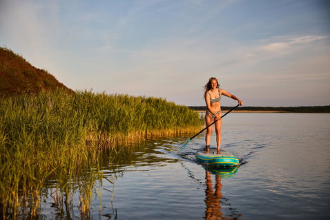 Duotone Fly Air aufblasbares SUP Board beim Stand Up Paddeln auf einem ruhigen See im Abendlicht