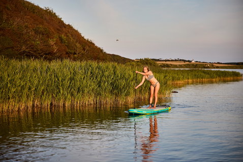 Duotone Fly Air aufblasbares SUP Board beim Stand Up Paddling auf ruhigem Gewässer bei Goldener Stunde
