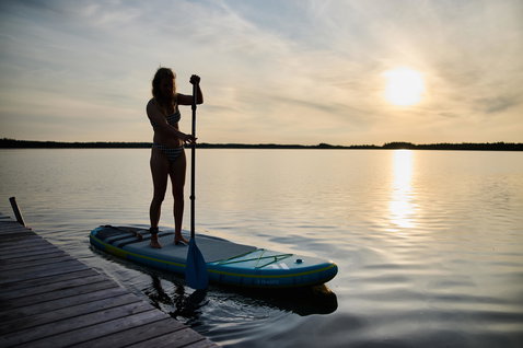 Duotone SUP Fly Air Premium aufblasbares SUP Board beim Stand Up Paddeln auf einem ruhigen See im Abendlicht