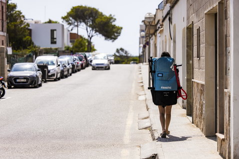 Duotone Fly Air inflatable SUP board carried as a backpack along a sunny Mediterranean street