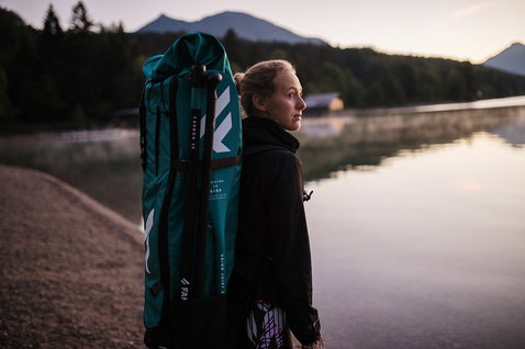 Fanatic SUP-Rucksack mit Carbon-Paddel, getragen von einer Frau an einem Bergsee in der Dämmerung