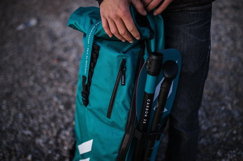 Fanatic Ray Air Pocket iSUP Reisetasche in türkis mit Carbon-SUP-Paddel beim Tragen im Freien