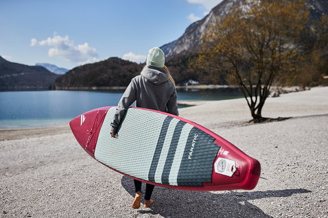Fanatic Falcon Air Premium inflatable SUP raceboard in red and mint carried toward an alpine lake