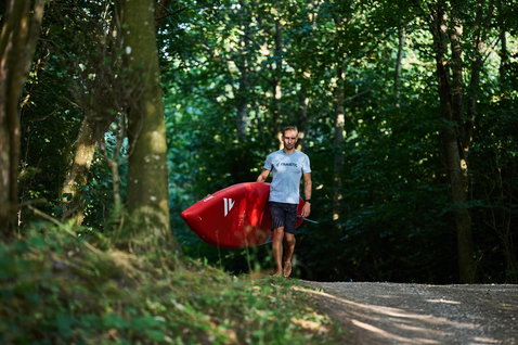 Duotone Ray Air aufblasbares Touring SUP-Board in rot, getragen auf einem Waldweg im Sommer