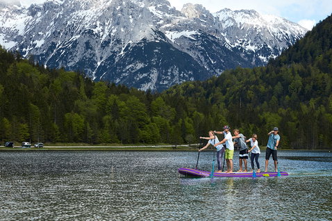 Fanatic Fly Air XL inflatable SUP board with five riders on an alpine lake with snow-capped mountains
