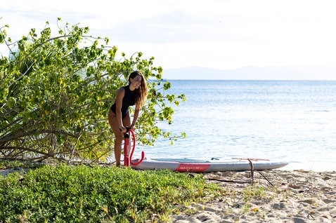 Fanatic Ray Air SLT inflatable SUP board being inflated on a tropical beach with red double-action pump