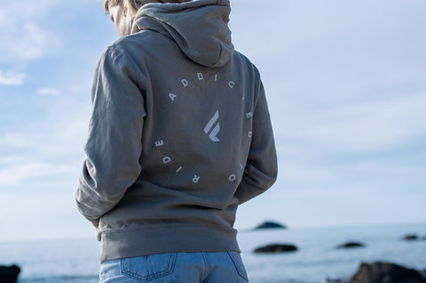 Fanatic unisex hoodie in stone grey with 'Addicted to Ride' back graphic at the coast