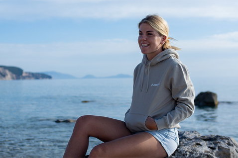 Fanatic SUP unisex hoodie in warm grey worn at a rocky coastal shoreline