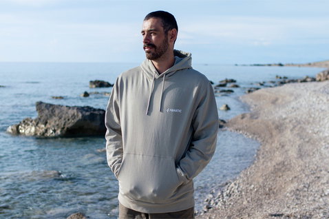 Fanatic unisex hoodie in stone grey worn at a rocky coastal beach