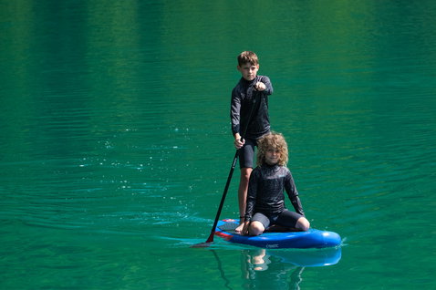 Fanatic Ripper Air SLT inflatable SUP board during paddling on a teal mountain lake with two young riders